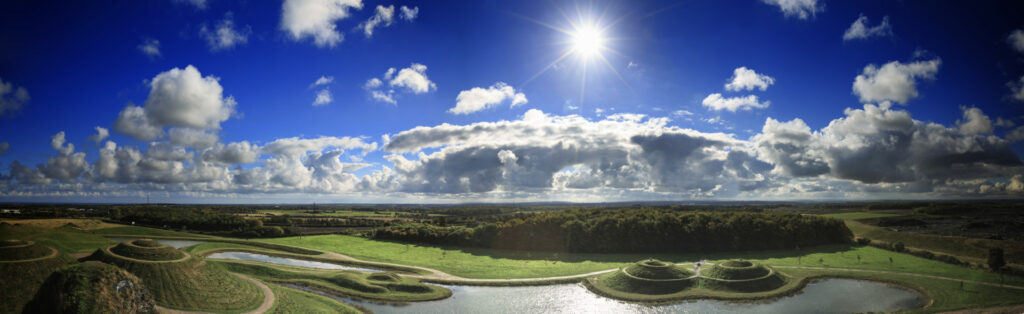 The sun is shining over a green field and a pond.
