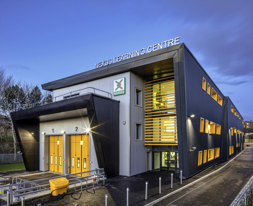 Exterior view of the nexus learning centre at twilight featuring a modern architecture with illuminated interiors and prominent signage.